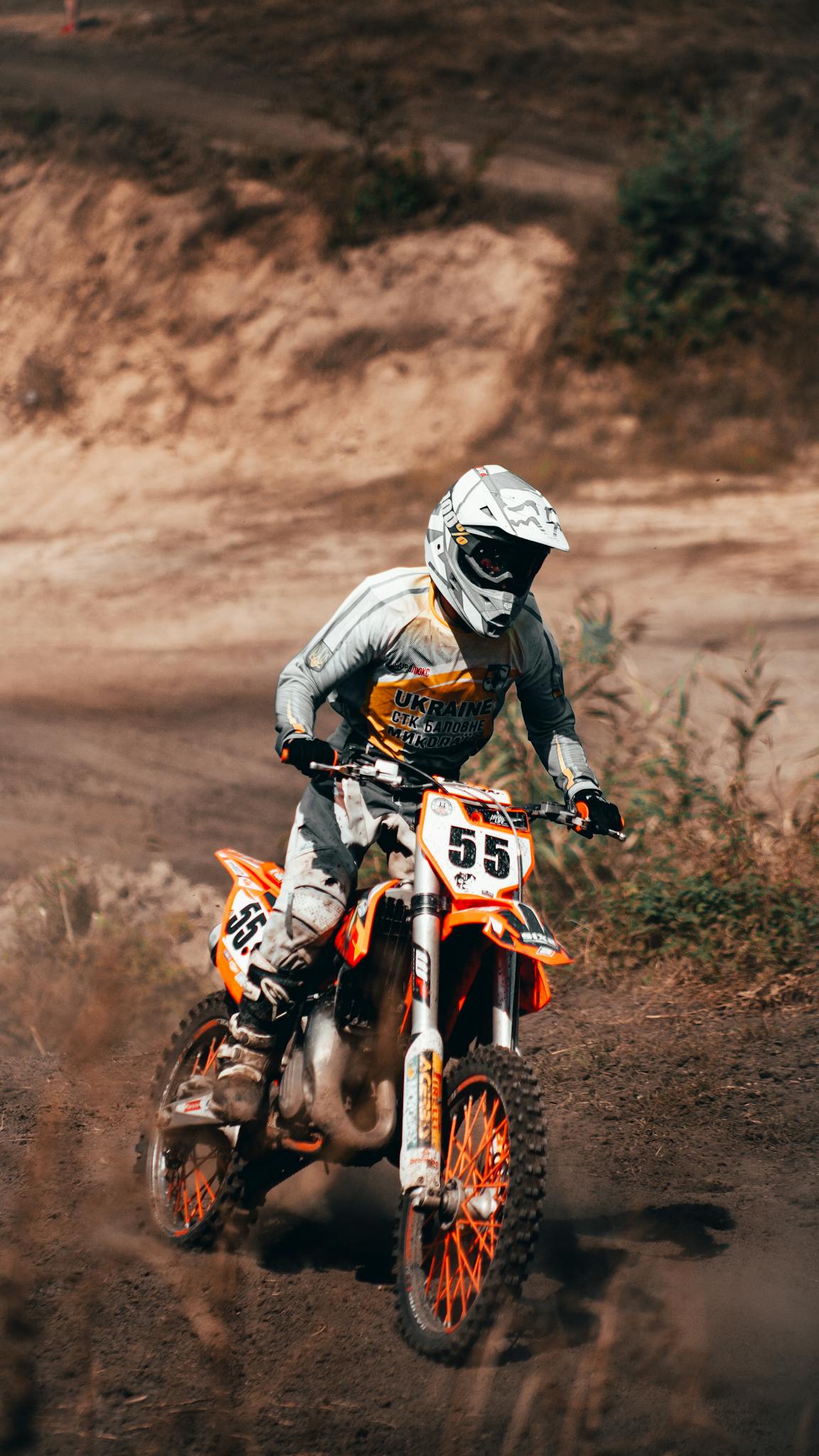 A motorcyclist in full gear races through rugged terrain, showcasing speed and skill.
